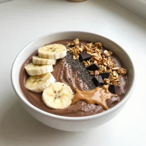 To make the Peanut Butter Chocolate Smoothie Bowl, you need a few key ingredients. Here&rsquo;s the list: - 2 ripe bananas, sliced and frozen - 1 cup unsweetened almond milk (or your milk of choice) - 2 tablespoons natural peanut butter - 2 tablespoons unsweetened cocoa powder - 1 tablespoon honey or maple syrup (optional for extra sweetness) - 1/2 teaspoon vanilla extract - Suggested toppings: sliced bananas, granola, chopped dark chocolate, chia seeds, drizzle of peanut butter These ingredients work together to create a creamy and rich smoothie bowl. The frozen bananas add a thick texture, while the cocoa powder brings a deep chocolate flavor. The natural peanut butter gives it a delightful nutty taste. If you want it sweeter, the honey or maple syrup is a great option. When it comes to toppings, feel free to get creative! Sliced bananas add freshness, while granola provides a nice crunch. Chopped dark chocolate adds a little indulgence. A drizzle of peanut butter on top makes it look fancy and delicious. Enjoy making this energizing treat! {{ingredient_image_2}} 1. First, gather your ingredients. You need frozen bananas, almond milk, peanut butter, cocoa powder, honey or maple syrup, and vanilla extract. 2. Next, combine all these ingredients in a blender. Make sure to add the frozen banana slices first. 3. Blend until smooth and creamy. If needed, stop to scrape down the sides. This helps mix everything well. 4. Once you reach the right texture, pour the smoothie into a serving bowl. You want it thick and inviting. - Layer your toppings artfully. Place sliced bananas, then granola, and add chopped dark chocolate. - Use colorful bowls. They make your smoothie bowl look even more fun and tasty. - Drizzle some peanut butter over the toppings for extra flavor and a nice look. Enjoy making your Peanut Butter Chocolate Smoothie Bowl! It's an energizing treat that is easy to make and fun to eat. To get the best texture for your smoothie bowl, frozen bananas are key. They add creaminess and chill to your mix. Always use ripe bananas. They taste sweeter and blend better. If your smoothie is too thick, you can adjust the liquid. Add a little more almond milk, one tablespoon at a time, until you reach your desired thickness. You can easily change the sweetness of your smoothie bowl. If you like it sweeter, add more honey or maple syrup. Start with a small amount, like half a tablespoon, and taste as you go. If you want a different option, try adding dates or a splash of vanilla. These can enhance the flavor without being too sweet. Pro Tips Use Frozen Bananas: Using frozen bananas not only enhances the creaminess of your smoothie bowl but also keeps it cold and refreshing without needing ice. Experiment with Sweeteners: Adjust the sweetness to your taste by trying different sweeteners like agave nectar or coconut sugar if honey or maple syrup isn&rsquo;t your preference. Layer for Texture: Layer different toppings to create a variety of textures in each bite. Consider adding nuts or seeds for a satisfying crunch! Customize Your Base: Feel free to switch up the base by adding spinach or protein powder for an extra nutrient boost without altering the delicious flavor. {{image_4}} You can change the taste of your smoothie bowl in fun ways. First, try adding protein powder or yogurt. This gives your bowl extra creaminess and boosts protein. You can use any flavor you like. Chocolate or vanilla protein powder works great! If you want to switch up the nut butters, feel free to use almond or cashew butter. Each nut butter adds a unique taste and texture. Almond butter has a light flavor. Cashew butter is creamy and smooth. Choose what you enjoy most! For a vegan-friendly option, use maple syrup instead of honey. All other ingredients are already vegan! You can also swap almond milk for coconut milk for a rich, creamy base. If you need gluten-free options, this recipe is safe! All the ingredients are gluten-free. Just check your toppings, as some granola may have gluten. Look for gluten-free labels to be sure. To keep your smoothie bowl fresh, store leftovers in the fridge. Use an airtight container to prevent air from getting in. This helps maintain its creamy texture. If you have toppings left, store them separately. Toppings can become soggy if mixed in. You can freeze the smoothie bowl for a quick treat later. Pour the smoothie into a freezer-safe container. Leave some space at the top, as it may expand when frozen. For defrosting, move it to the fridge overnight. You can also let it sit at room temperature for about 30 minutes. Stir it well before serving. If it seems thick, add a splash of almond milk and blend it again for a smooth texture. You can use many types of milk instead of almond milk. Here are some options: - Soy milk - Oat milk - Coconut milk - Regular cow's milk Each type can change the flavor a bit, so choose what you like best. Yes, you can! Here are some tips for pre-preparation: - Blend the smoothie and store it in the fridge for up to 24 hours. - Keep the toppings separate until you're ready to eat. - Stir just before serving to regain a creamy texture. You can boost nutrition by adding these superfoods or seeds: - Chia seeds for fiber and omega-3s - Flaxseeds for extra healthy fats - Spinach for a green boost - Protein powder for added protein These additions help you create a more balanced meal while keeping it tasty! This blog post showed you how to make a tasty smoothie bowl. We covered all the key ingredients and step-by-step instructions to blend it all together. I shared tips for a perfect texture and easy ways to adjust sweetness. You can add your favorite flavors and make it fit your diet. Plus, you learned how to store it well. Enjoy creating your smoothie bowl, and don't be afraid to experiment with toppings and flavors! Your kitchen adventures await.